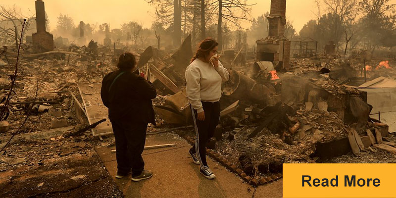 Two women examine the wreckage of wildfire destroyed homes
