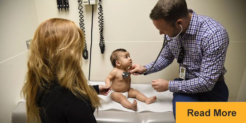 physician examining baby with stethoscope in exam room