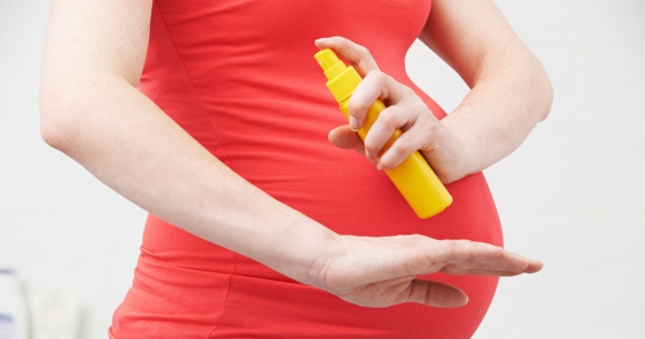 pregnant woman applying insect repellent to arm