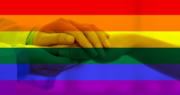 physician holding patients hand with pride flag behind