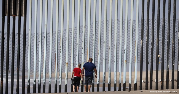 Man and child look through border fence
