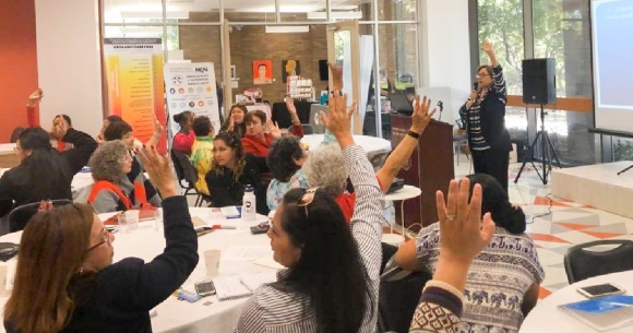 Participants raise hands as part of presentation at 5th annual women's conference