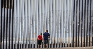Man and child look through border fence