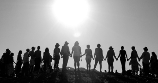 People stand on ridge holding hands with sun above