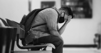 A man in a mask holds his head in grief