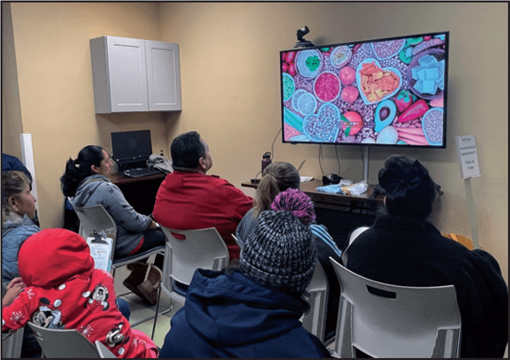 Participants and their family members watch videos on making healthy plant-based meals while waiting to consult with a clinician.